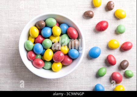 Candy coated milk chocolate peanuts, in a white bowl, on linen fabric. Roasted peanuts, coated with milk chocolate, coated with multicolored sugar. Stock Photo