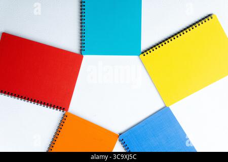 Flat lay photo of colorful spiral notebooks arranged in a circular pattern on white background. Stock Photo