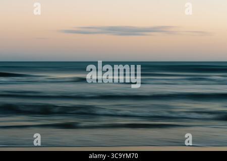 Calm ocean waves beneath a pastel-colored evening sky. Stock Photo