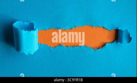Hole ripped in blue paper on orange background. Copy space. Stock Photo
