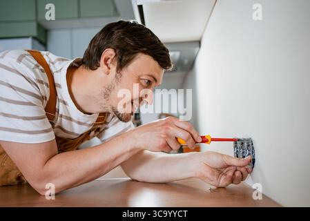 Electrician installing a new electrical socket in a modern kitchen, using a screwdriver to securely attach the fixture to the wall with precision and expertise Stock Photo