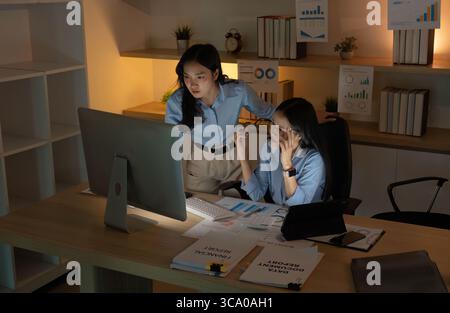 Late Night Work. Two women collaborating on data analysis in a dimly lit office. Stock Photo