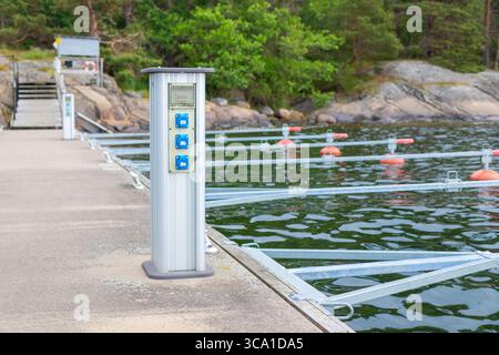 Charging station for boats at a marina pier in Finland, with electrical outlets powering sailboats and motorboats docked near the shore on a sunny sum Stock Photo