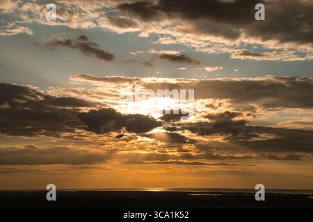 Dramatic sunset over the Baltic Sea with golden sun rays breaking through dark clouds, creating a warm glow on the horizon. Nature landscape photograp Stock Photo