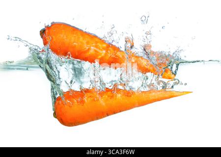 Carrots plunging into clear water, creating dynamic splashes and droplets, showcasing freshness and vitality. Stock Photo