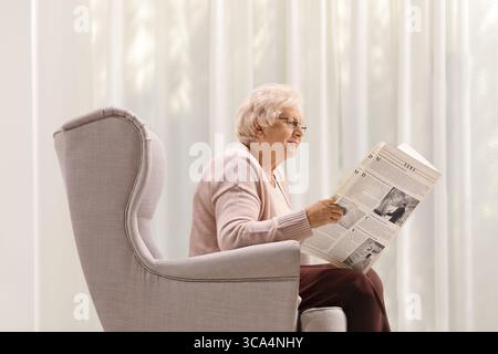 Elderly lady reading a newspaper seated in an armchair Stock Photo