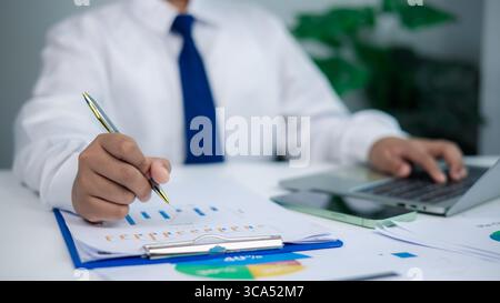 Professional businessman analyzing financial data and graphs on clipboard with laptop, representing business analysis, data management, market researc Stock Photo