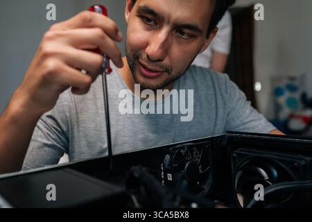 Close-up face of skilled technician disassembling desktop computer using precision screwdriver while performing intricate hardware diagnostic and Stock Photo