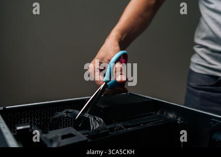 Close-up of technician hand using scissors to cut cable inside desktop computer, performing maintenance or repair work on complex internal components. Stock Photo