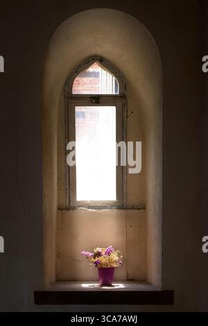 Dried flowers in the incoming sunlight on the ledge of a very old, narrow, dirty window Stock Photo