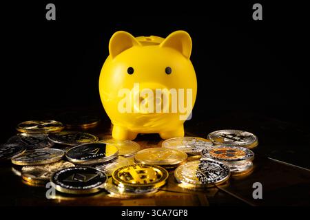 A yellow piggy bank surrounded by silver and gold Bitcoin coins on a black surface. The image symbolizes digital currency, financial savings, and inve Stock Photo