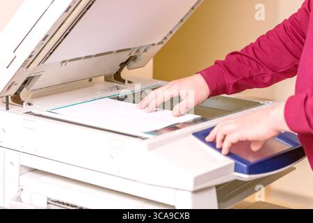 Man putting paper sheet on printer for scanning. Office work concept Stock Photo