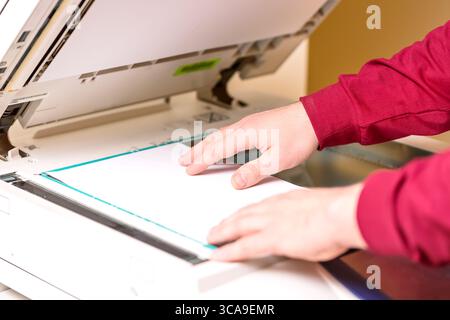 Man putting paper sheet on printer for scanning. Office work concept Stock Photo