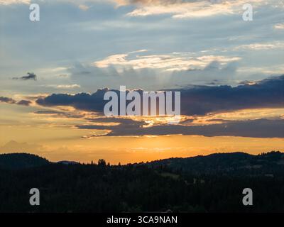 Warm sunset light breaks through layered clouds, casting golden tones across distant forested hills and valleys Stock Photo