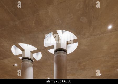 a modern architectural interior. Massive concrete columns support a raw concrete ceiling, crowned with large circular skylight. Stock Photo
