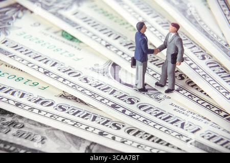 Business deal or agreement and success concept. Two miniature businessmen shaking hands while standing on american dollar money background Stock Photo