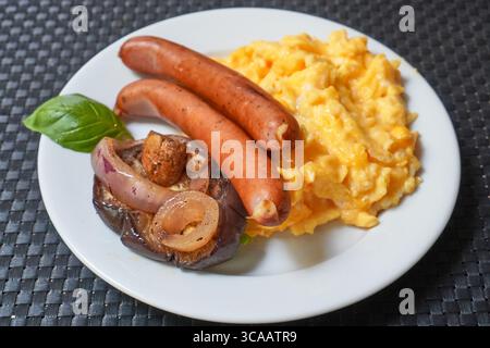 Sausages served with scrambled eggs, garnished with greens and tomato. Stock Photo