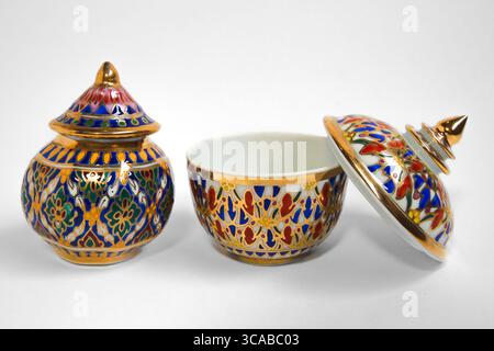 Two vintage Thai Benjarong porcelain cups with lids, gold rims, and floral patterns in blue and red, isolated on white background. Stock Photo