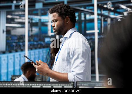 Manager walking through data center electronics providing processing resources for different workloads. Team leader using tablet to evaluate server rigs tasked with solving complex operations Stock Photo