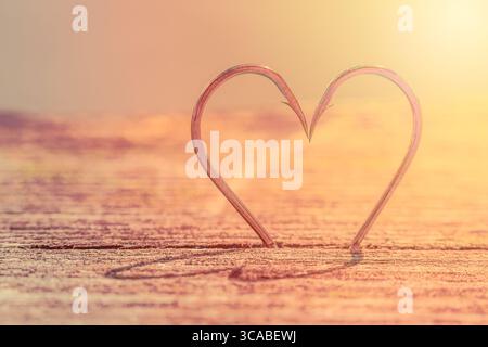 Heart Shape Made of Two Fish Hooks with shadows on wood Stock Photo