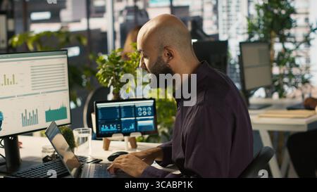 Employee in office celebrating achievement while looking at laptop screen, expressing excitement over successful results. Man happy about positive business accomplishment, camera A Stock Photo