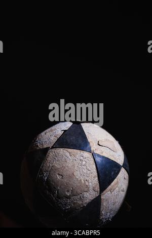 Damaged yellow, black, and white soccer ball against a black background Stock Photo