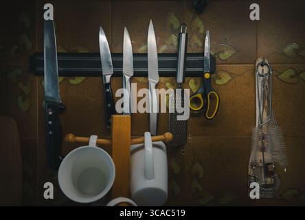 Kitchen knives and other accessories on a magnetic strip on the wall with decorative tiles. Stock Photo