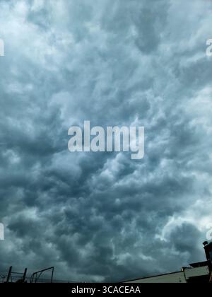 Menacing dark clouds enveloping the sky, casting a dramatic atmosphere over urban buildings and creating an ominous cityscape Stock Photo