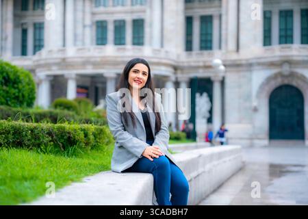 Confident young happy business Latina woman with long straight hair, gray blazer, dark top and blue pants, smiling while walking in Mexico City near i Stock Photo