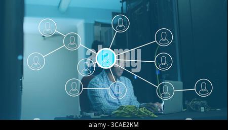Typing IT technician working on laptop in data center, with Ethernet cables and server racks Stock Photo