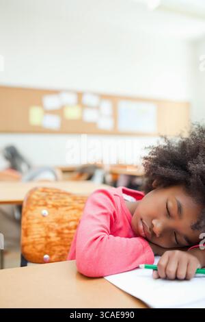 African American girl resting head on arms at classroom desk with green pencil, paper, copy space Stock Photo