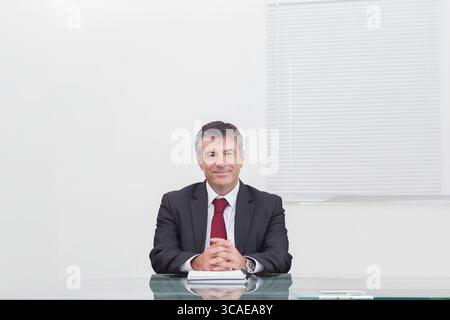 Senior man placing hands wearing wristwatch on closed notebook at transparent glass desk in office Stock Photo