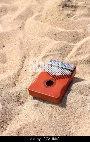 A wooden kalimba rests on golden sand, showcasing its metallic tines glinting in sunlight. The smooth surface contrasts with the textured grains aroun Stock Photo