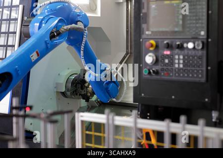 Robot loading parts into CNC lathe machine. Automated process of loading parts into CNC lathe machine with robotic arm. Selective focus. Stock Photo