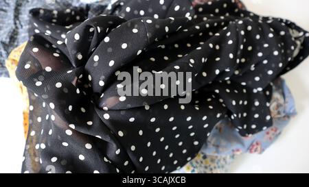Photo of crumpled fabric. Black fabric with white polka dots. Chaotic folds. In the background, a blur of fabric of different colors. White background Stock Photo