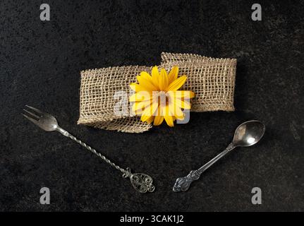 This captivating top view image features an abstract composition that blends vintage spoon and fork, a textured burlap ribbon, and a delicate yellow f Stock Photo
