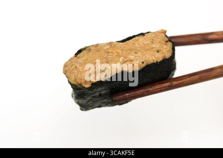 Closeup of a single, perfectly crafted sushi gunkan maki, featuring rice, nori, and tuna salad, held delicately by chopsticks. Stock Photo