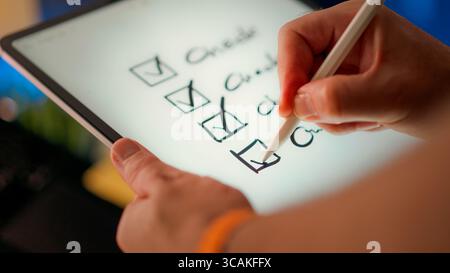 Digital checklist marked tasks completion on tablet screen with stylus. Close-up view of hand ticking checkboxes representing progress, organization a Stock Photo