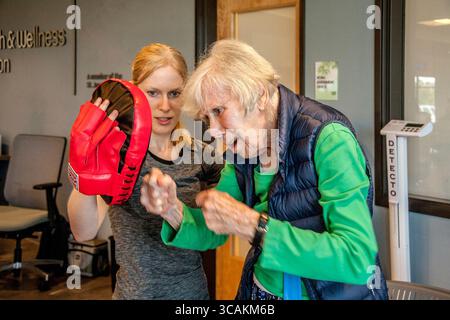 July 19, 2017, Huntington Beach, California: An enthusiastic 87-year-old woman practices boxing punches with an instructor holding a training glove at a senior center gymnasium in Huntington Beach, CA. (Credit Image: © Spencer Grant/ZUMA Press Wire) Stock Photo