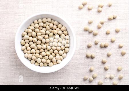 Dried green peas in white bowl on linen. Seeds of Pisum sativum, a pulse, vegetable and fodder crop, that can be reconstituted in hot water. Stock Photo