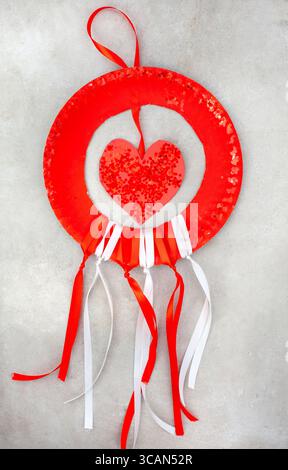 red paper plate with hanging heart with glitter. the bottom has red and white ribbons hanging from it Stock Photo