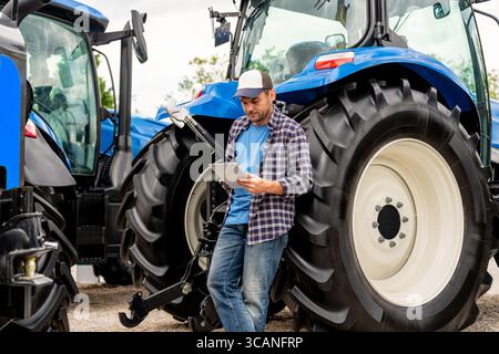 Male farmer using digital tablet near agricultural tractors Stock Photo