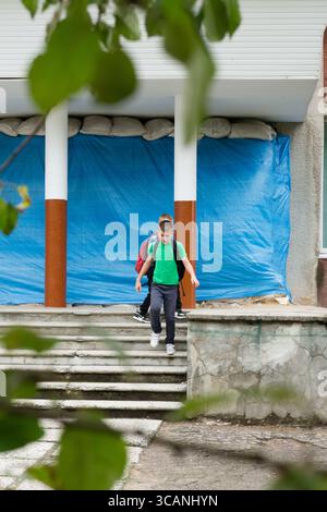 Two school children with backpacks are walking down the steps of a building. The building is covered with a blue tarp and sandbags. The setting convey Stock Photo