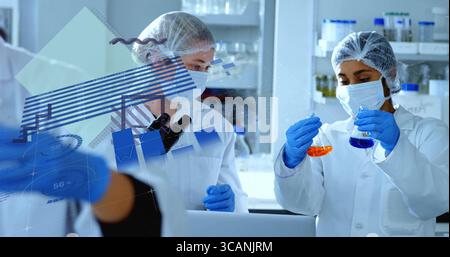 Holding colored flasks, two scientists in lab coats analyzing results in research lab, with tablet Stock Photo