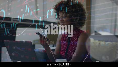 Woman wearing red blouse analyzing charts on laptop in living room, smartphone, coffee cup Stock Photo