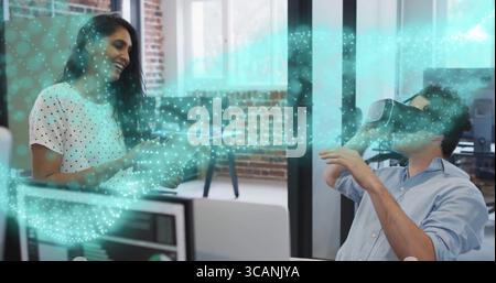 Coworkers collaborating with clipboard, wearing VR headset in office with monitors showing hologram Stock Photo