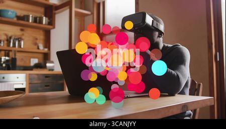 Exploring virtual space man wearing VR headset using laptop in kitchen, with colorful bokeh Stock Photo