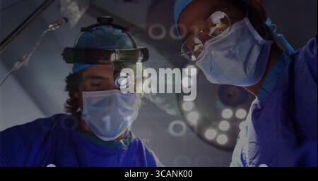 Two surgeons in blue scrubs operating in operating room, with overhead light and digital overlays Stock Photo