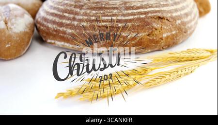 Showing artisan loaf with two rolls, wheat stalks on white table, Merry Christmas 2017 graphic Stock Photo