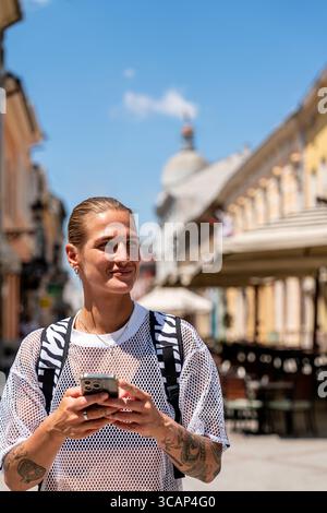 Stylish solo traveler using smartphone while walking through city in summer Stock Photo
